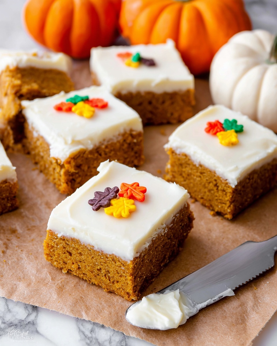 The image shows six square pumpkin bars on brown parchment paper, each with two layers: a thick, moist orange-brown pumpkin base and a smooth, creamy white frosting on top. Some bars have small, colorful leaf-shaped sprinkles in red, green, yellow, orange, and purple on one corner of the frosting. Next to the bars is a shiny silver knife with a white creamy spread on its blade. There are two small pumpkins in the background, one orange and one white, placed on a white marbled textured surface. The photo taken with an iphone --ar 4:5 --v 7