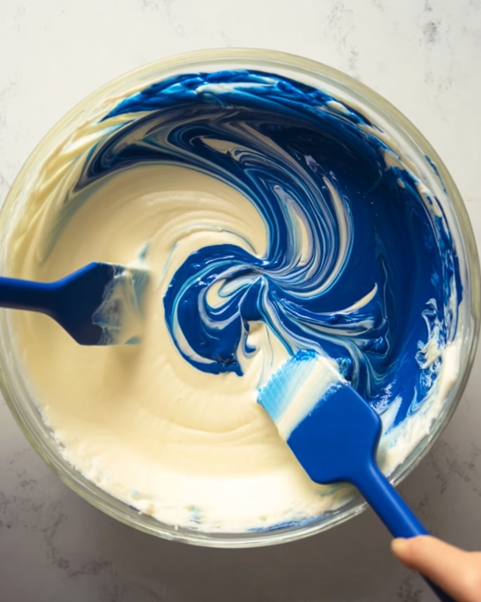 A large round clear bowl filled with smooth, thick white cream as the base layer. On top of this is a blob of dark blue liquid dye being mixed in with two blue spatulas, one on the left and one on the right, both held by a woman's hand. The white cream and blue dye create swirling patterns in the bowl, showing a blend of the two colors in motion. The bowl sits on a white marbled surface. photo taken with an iphone --ar 4:5 --v 7