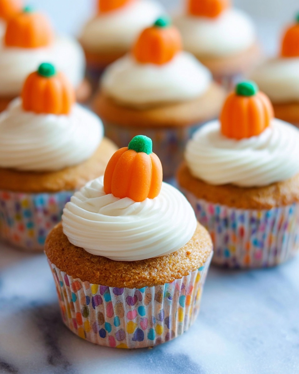 The image shows several cupcakes arranged in a group on a white marbled surface. Each cupcake has one layer of light brown cake with a soft, slightly rough texture. On top of each cupcake is a swirl of smooth white frosting, thick and creamy, forming a small peak in the center. Sitting on the peak of each frosting swirl is a bright orange candy shaped like a small pumpkin with a green top. The cupcakes are inside patterned paper liners with various small colorful spots. The photo focuses on the closest cupcake, with others softly blurred in the background. Photo taken with an iphone --ar 4:5 --v 7