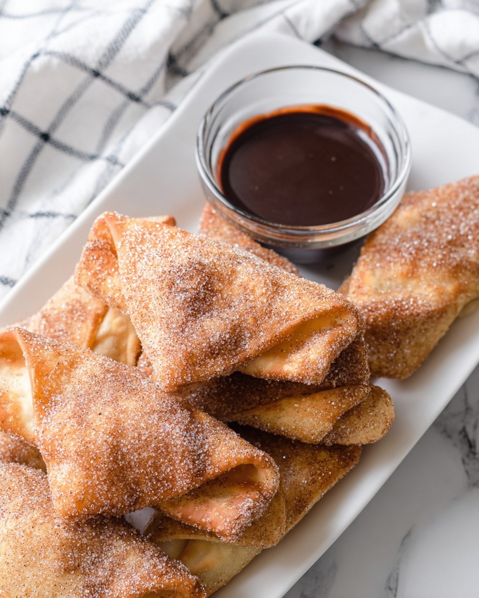 A white rectangular plate on a white marbled surface holds several golden-brown, folded pastries covered in a light sprinkle of sugar and cinnamon. The pastries have a thin, crispy outer texture with some areas showing the soft, light inside. Next to the pastries is a small, clear glass bowl filled with dark chocolate sauce. The scene includes part of a white cloth with a blue checkered pattern in the background. Photo taken with an iphone --ar 4:5 --v 7