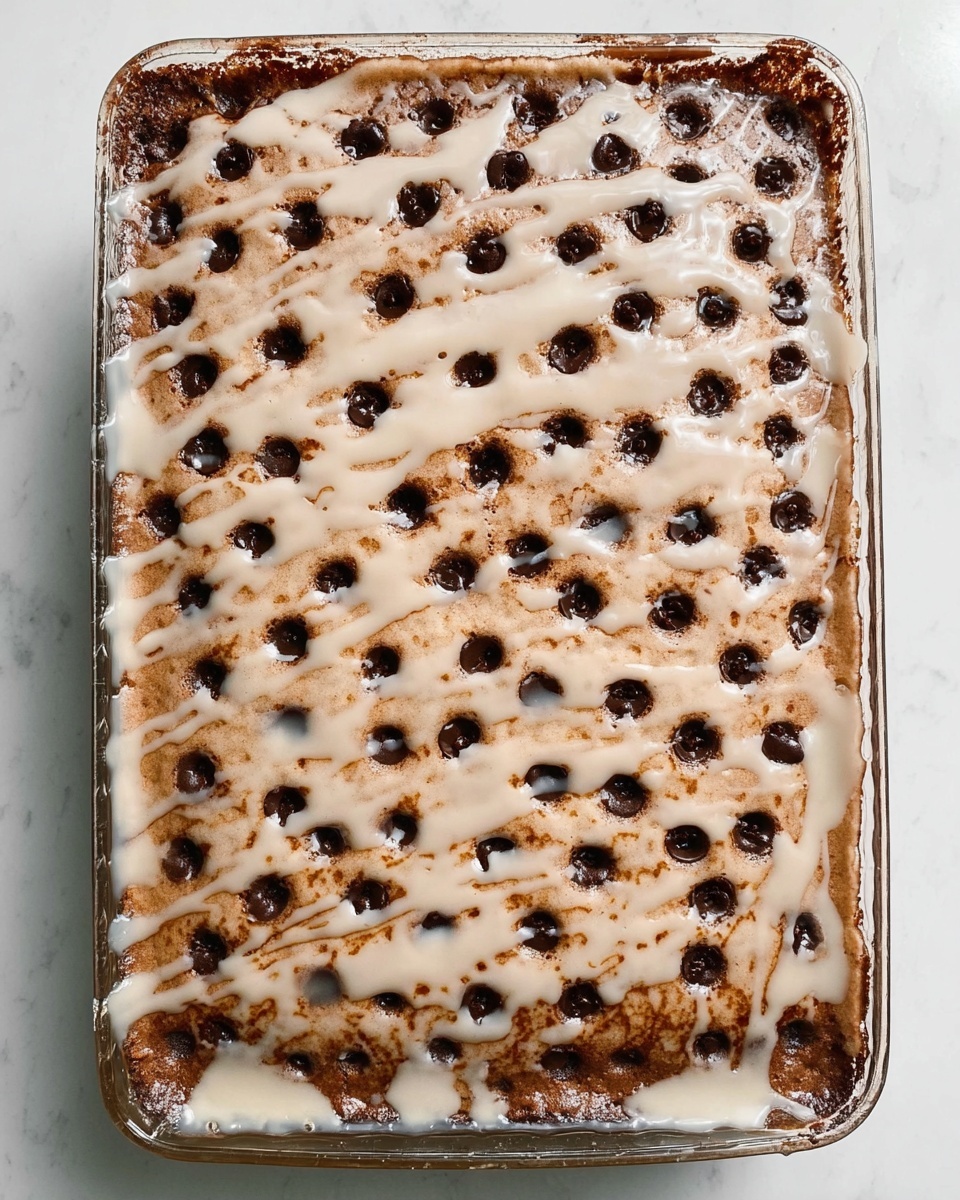 A rectangular baked chocolate dessert with a light brown, soft top layer, dotted with many small, dark brown holes across the surface. A shiny, white glaze is drizzled unevenly over the top, adding contrast and texture. The dessert rests in a clear glass baking dish on a white marbled surface. Photo taken with an iphone --ar 4:5 --v 7