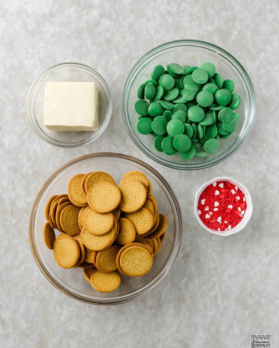 Four clear glass bowls are placed on a white marbled surface. The largest bowl at the bottom left is filled with many whole golden sandwich cookies stacked together. Above it to the right is a medium-sized bowl filled with round, flat green candy melts. At the top left is a small bowl containing a block of cream cheese with a smooth texture. To the right of the candy melts is a tiny white bowl filled with small red heart-shaped sprinkles. The composition is bright and neatly arranged, photo taken with an iphone --ar 4:5 --v 7