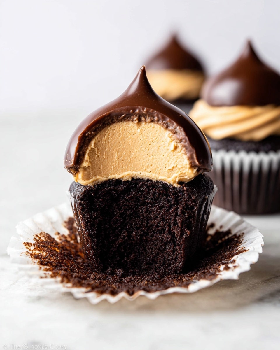 The image shows a close-up of a chocolate cupcake with two more cupcakes blurred in the background. The cupcake in front has its white paper wrapper opened and peeled down, revealing a dark, moist chocolate cake base as the bottom layer. On top of the cake is a thick, fluffy peanut butter cream layer in light brown color, shaped in a smooth dome. This cream layer is fully coated with a shiny, dark chocolate shell that forms a rounded peak at the top. The background has a clean white marbled texture. Photo taken with an iphone --ar 4:5 --v 7