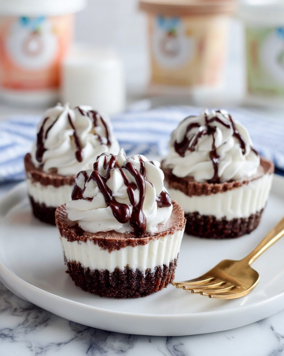 Three small dessert cups sit on a white plate. Each cup has three layers: the bottom layer is dark brown and crumbly, the middle layer is white and smooth, and the top layer is a fluffy white cream shaped with swirls. On top, dark brown chocolate sauce is drizzled over the cream. A gold fork rests on the right side of the plate. The background shows a white marbled surface and blurred containers and fabric. Photo taken with an iphone --ar 4:5 --v 7