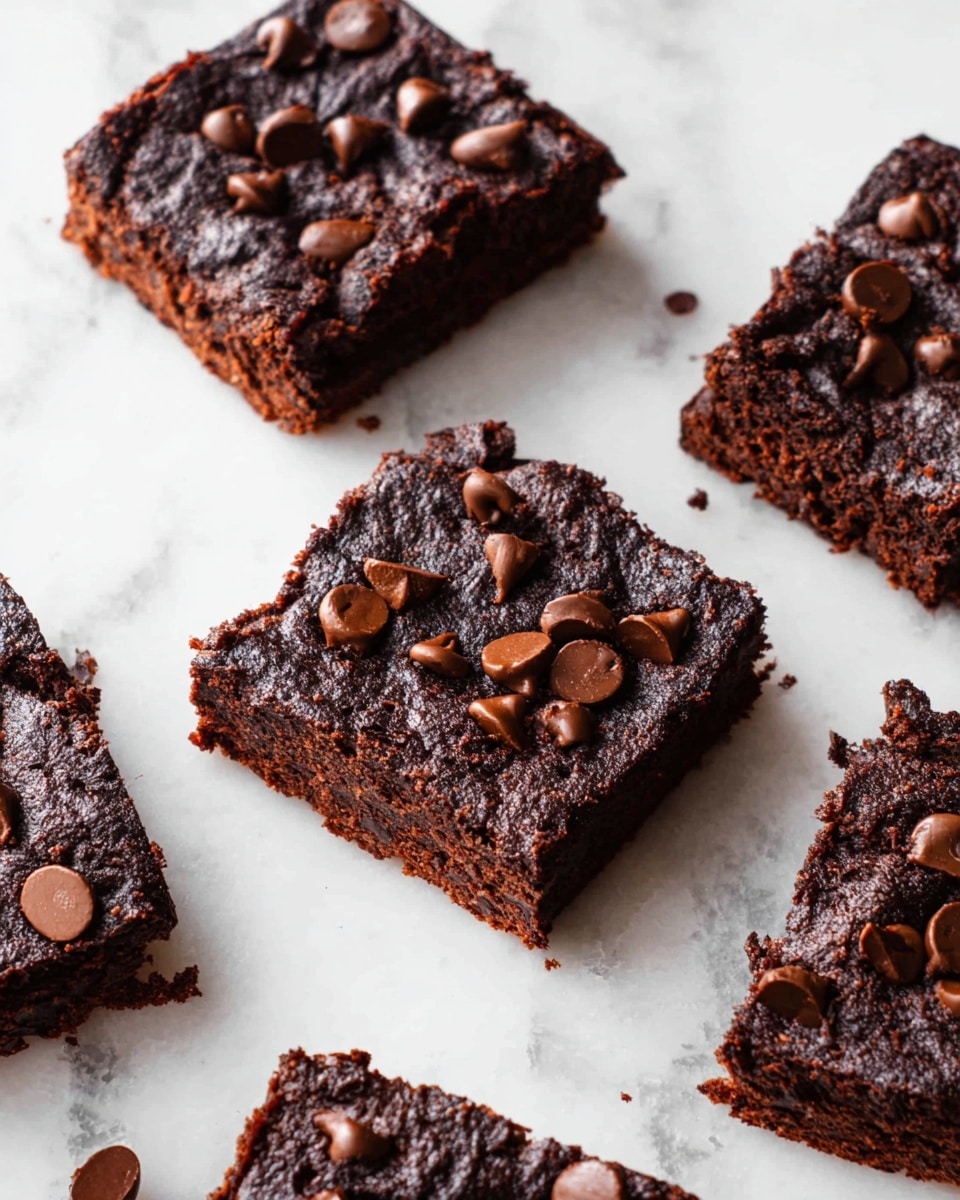 The image shows several square dark brown brownies with a slightly rough texture arranged on a white marbled surface. Each brownie has a layer of melted chocolate chips scattered unevenly on the top, creating a mix of smooth and slightly shiny spots contrasted with the matte base. The brownies appear thick and dense, and some edges look a bit crumbly. The scene is bright with natural light highlighting the rich chocolate tones. photo taken with an iphone --ar 4:5 --v 7