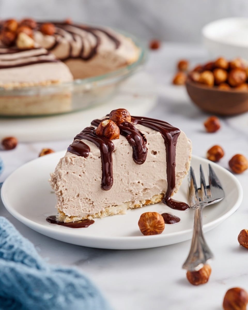 A slice of light brown mousse pie with a creamy texture and a thin, slightly crumbly crust at the bottom sits on a white plate. The pie slice is drizzled with dark chocolate sauce on top, with some sauce flowing down the sides. Around the plate are whole hazelnuts scattered randomly. A silver fork rests beside the pie slice on the right. In the background, there is a bowl filled with hazelnuts and a full pie with chocolate drizzle visible, all placed on a white marbled surface. A bit of a blue cloth is seen in the bottom left corner. The scene is softly lit and looks fresh. photo taken with an iphone --ar 4:5 --v 7