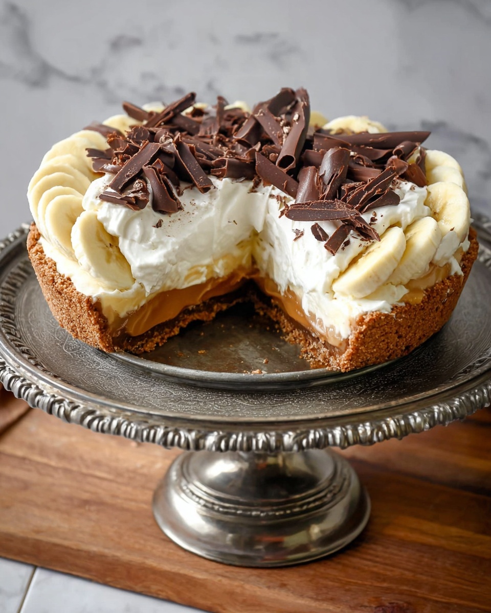 A pie with four visible layers sits on an ornate metal stand: at the bottom is a crumbly brown crust, above that is a smooth caramel layer, next is a layer of banana slices arranged circularly along the edge, topped with a thick, fluffy white cream layer, and the pie is finished with dark brown chocolate curls and shavings scattered across the cream. The pie has one slice removed, showing the inside layers clearly, and the stand rests on a wooden surface with a white marbled background. photo taken with an iphone --ar 4:5 --v 7