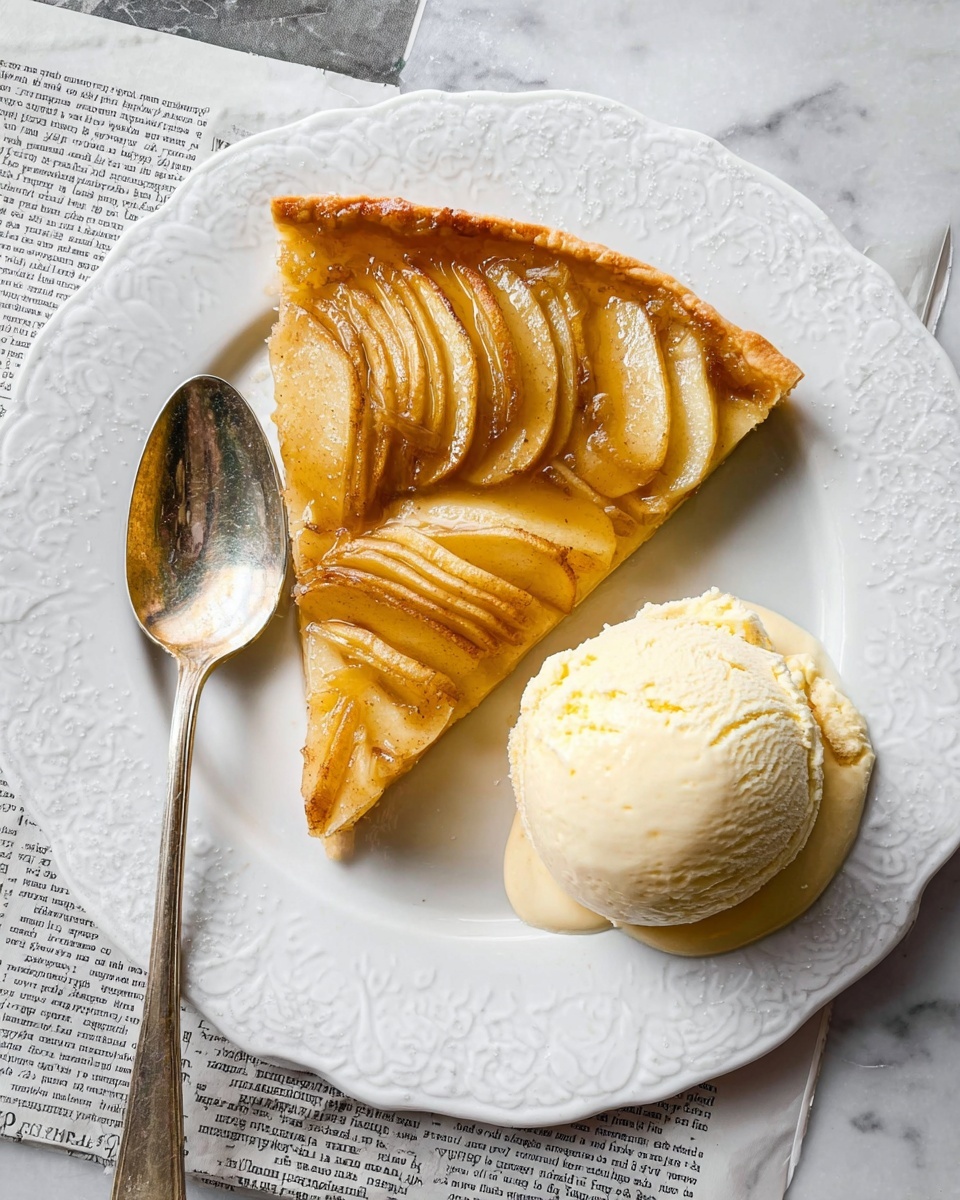 A white plate with a decorative edge holds a slice of apple tart and a large scoop of pale cream-colored ice cream on the right side. The tart slice has a thin bottom crust and a glossy, golden layer of thinly sliced apples arranged in slightly overlapping rows covering the entire top. The apples show a warm yellow-brown color with some caramelized edges. A shiny silver spoon with a long handle rests on the left side of the plate. The plate is set on a white marbled surface with a piece of newspaper partially visible underneath the plate. photo taken with an iphone --ar 4:5 --v 7
