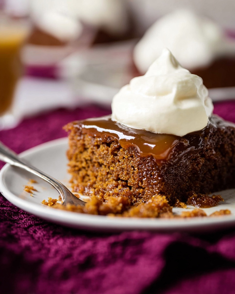 The image shows a piece of brown cake with a thick, moist texture with a glossy syrup glaze covering the top layer. On top of the syrup is a dollop of smooth, white whipped cream, softly piled. The cake sits on a white plate placed on a deep purple cloth, with some cake crumbs scattered around. In the background, a blurred spoon rests on the plate and parts of other dishware are faintly visible on a white marbled surface. photo taken with an iphone --ar 4:5 --v 7