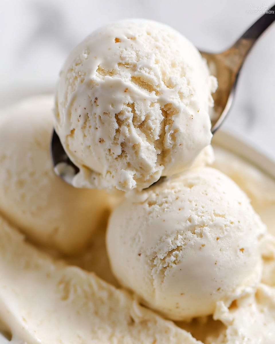The image shows three scoops of creamy vanilla ice cream with a smooth, slightly melting texture. Each scoop is off-white with tiny specks of vanilla visible throughout, showing some rough and soft surfaces. A metal spoon holds one of the scoops, lifting it slightly above the others, with a bit of ice cream melting onto the spoon’s edge. The background is a white marbled texture, keeping the focus on the ice cream. photo taken with an iphone --ar 4:5 --v 7