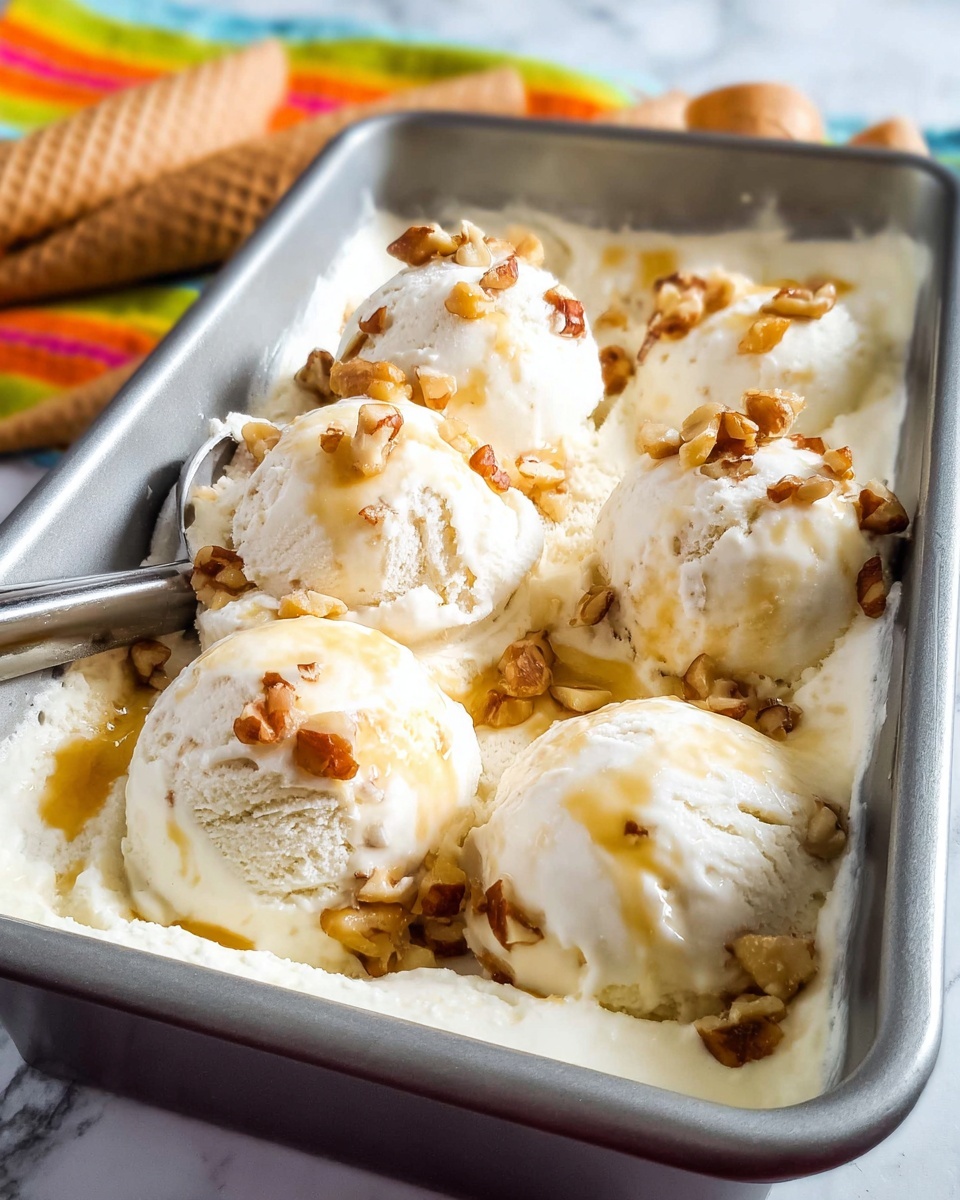 The image shows a metal rectangular pan filled with creamy white ice cream scoops. Each scoop is topped with small brown nuts scattered unevenly and drizzled with light golden syrup. The ice cream looks smooth with some soft texture, and the nuts add a crunchy contrast on top. In the background, there is a colorful striped cloth and some waffle cones visible, all set on a white marbled surface. The scoops are closely packed, filling the pan fully, and the overall scene is bright and inviting. photo taken with an iphone --ar 4:5 --v 7
