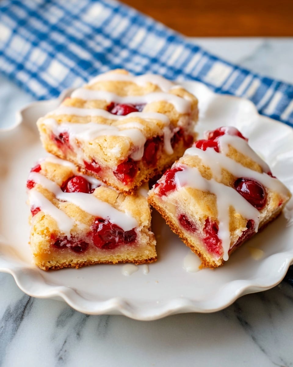 Three square pieces of dessert bars sit on a white plate with scalloped edges. Each bar has three layers: a light golden-brown crust at the bottom, a bright red cherry filling in the middle with whole cherries visible, and a pale golden lattice top layer. A creamy white glaze is drizzled over the top, slightly dripping onto the plate. The plate rests on a surface with a white marbled texture, and a blue and white cloth is partially visible in the background. photo taken with an iphone --ar 4:5 --v 7
