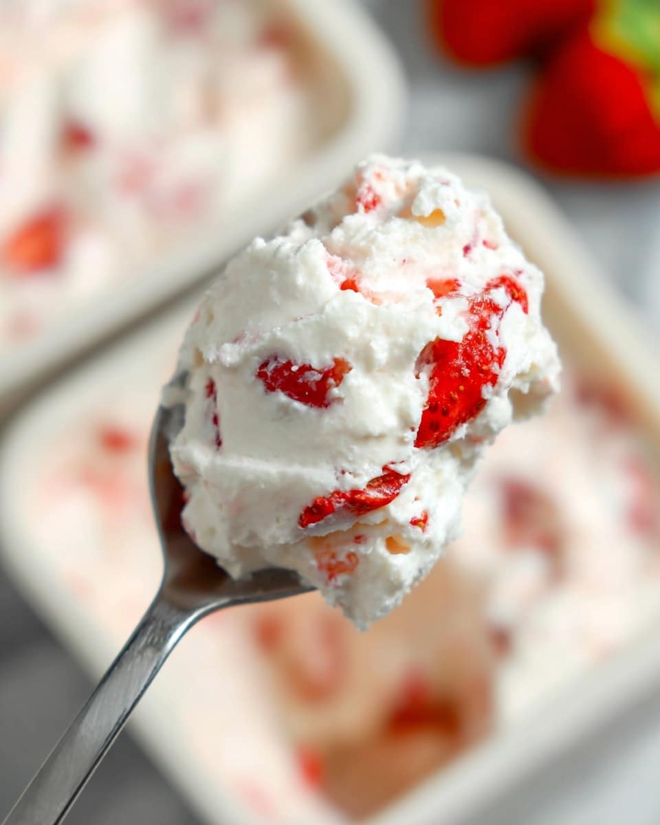 A close-up view of a spoon holding a scoop of creamy white mixture with small red strawberry pieces mixed inside, showing soft and fluffy texture with juicy chunks of strawberries. The background has a blurred white marbled texture and hints of more strawberry and creamy mix in white containers. The spoon is metal with a simple design, angled diagonally to the top right. photo taken with an iphone --ar 4:5 --v 7