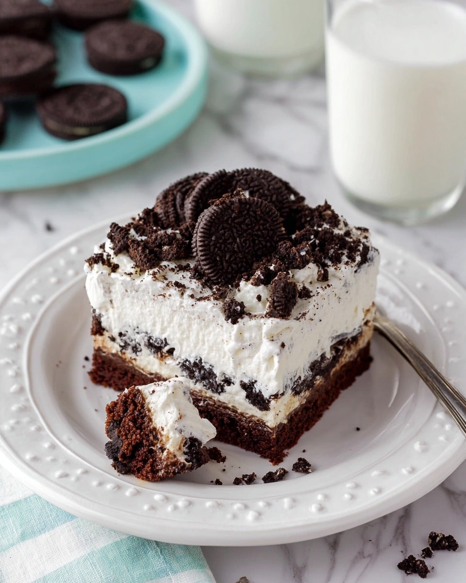 This image shows a square piece of cake on a white plate with a decorative edge. The cake has three visible layers: a dark brown chocolate base, a white creamy middle layer with pieces of cookies, and a thick white whipped cream top layer. The top is covered with crumbled and broken dark chocolate cookies with white cream filling. The plate sits on a white marbled surface, with a glass of milk to the upper right, a light blue plate with a ring of whole dark chocolate cookies in the background on the upper left, and a small fork with a bite-sized piece of cake holding a mix of all layers near the bottom left. photo taken with an iphone --ar 4:5 --v 7