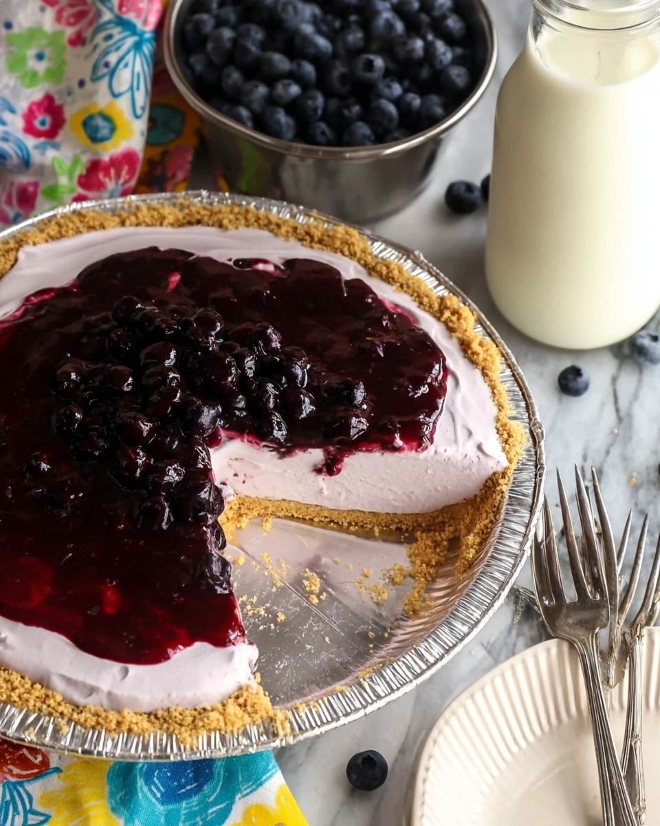 The image shows a pie with three visible layers: a crumbly golden brown crust at the bottom and sides, a thick pale pink creamy layer in the middle, and a shiny dark purple berry topping with whole berries on top. The pie is inside a clear foil pie pan. Around the pie, a white marbled surface is visible with a small metal bowl filled with dark blue berries in the top background, a glass jar filled with white milk to the right, and a white textured plate at the bottom right corner. Two silver forks rest on a colorful cloth with floral patterns near the pie photo taken with an iphone --ar 4:5 --v 7