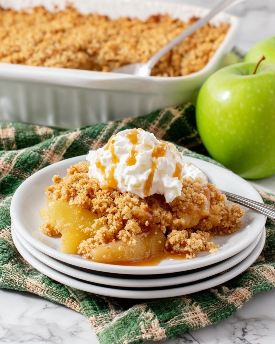 A white plate stacked on two similar plates holds a serving of apple crumble with a crumbly golden brown topping and soft cooked apple slices beneath. The crumble has a rough, uneven texture with visible small chunks. On top, there is a dollop of white whipped cream lightly drizzled with caramel sauce. A silver spoon rests in the crumble on the plate. Behind the plate, a larger white baking dish is filled with more apple crumble with the same textured topping. A green apple is placed to the right and left of the plates on a green and white checkered cloth, all set on a white marbled background. Photo taken with an iphone --ar 4:5 --v 7