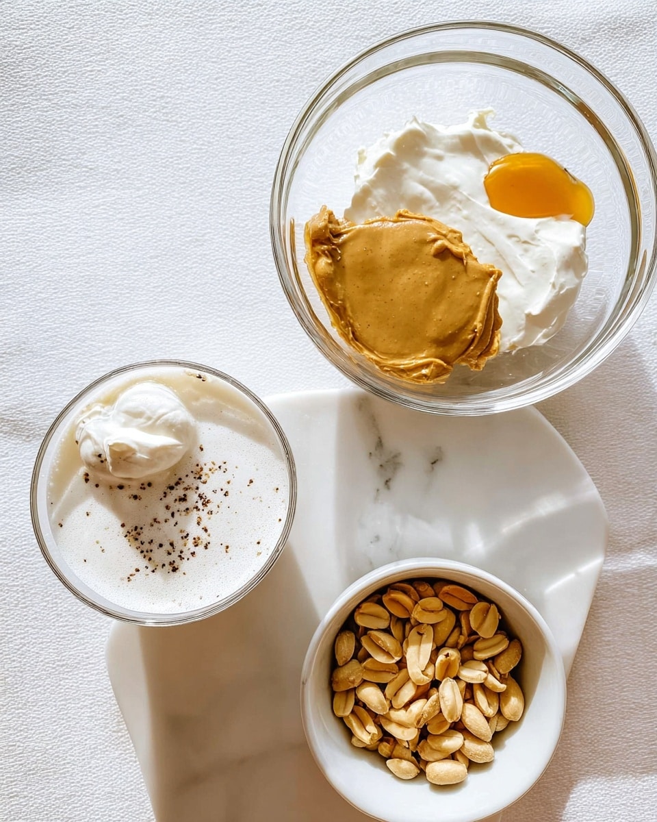 The image shows three clear glass bowls placed on a white marbled surface. The largest bowl at the top right contains four layers of ingredients: a creamy white layer of what looks like cream cheese or yogurt, a thick light brown layer of peanut butter, a small dollop of smooth golden honey on the right edge, and another creamy white dollop on top. Below and to the left is a smaller clear glass bowl filled with a frothy white liquid resembling milk foam, topped with some black specks, possibly spices. At the bottom right is a white bowl filled with dry roasted peanuts, showing their light brown skins and rough texture. The overall scene is bright and clean with soft natural lighting. photo taken with an iphone --ar 4:5 --v 7