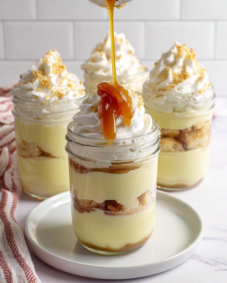 This image shows four clear glass jars filled with layered dessert placed on a white marbled surface. Each jar contains three layers of smooth, pale yellow pudding separated by layers of light brown cake pieces. The top layer is a swirl of white whipped cream, sprinkled with small golden cake crumbs. In the front jar, golden caramel sauce is being poured over the whipped cream, adding a shiny, rich texture. The jars are set on a white plate, and the background has a white tiled wall with three jars in soft focus behind the main one. photo taken with an iphone --ar 4:5 --v 7
