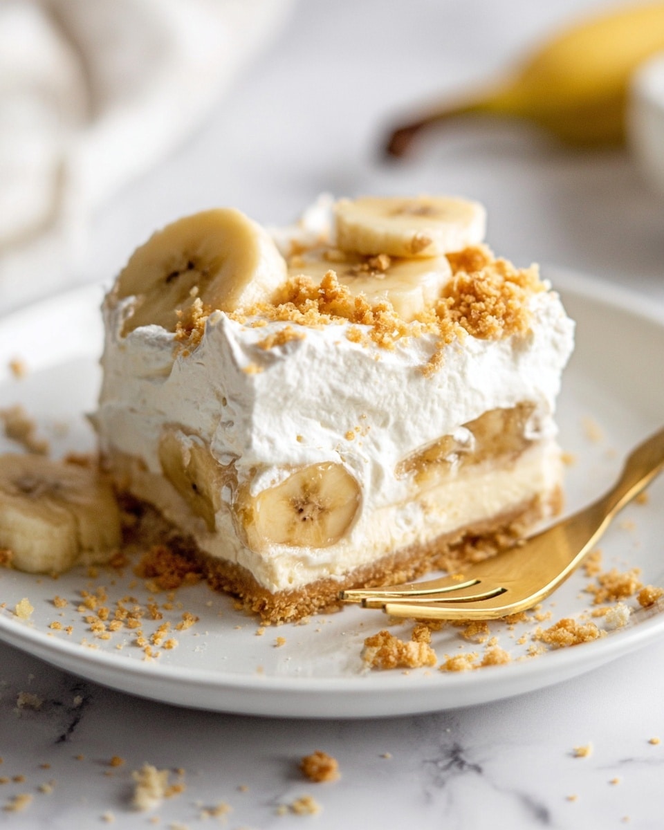 A square piece of dessert sits on a white plate on a white marbled surface, showing three layers: a light, crumbly base, a thick middle layer with banana slices visible inside, and a top layer of fluffy white cream with more banana slices and crumbled crumbs sprinkled on top. A golden fork rests on the plate next to the dessert with some crumbs scattered around. The photo is taken close up with soft natural light coming from the left side, making the cream look smooth and airy. Photo taken with an iphone --ar 4:5 --v 7