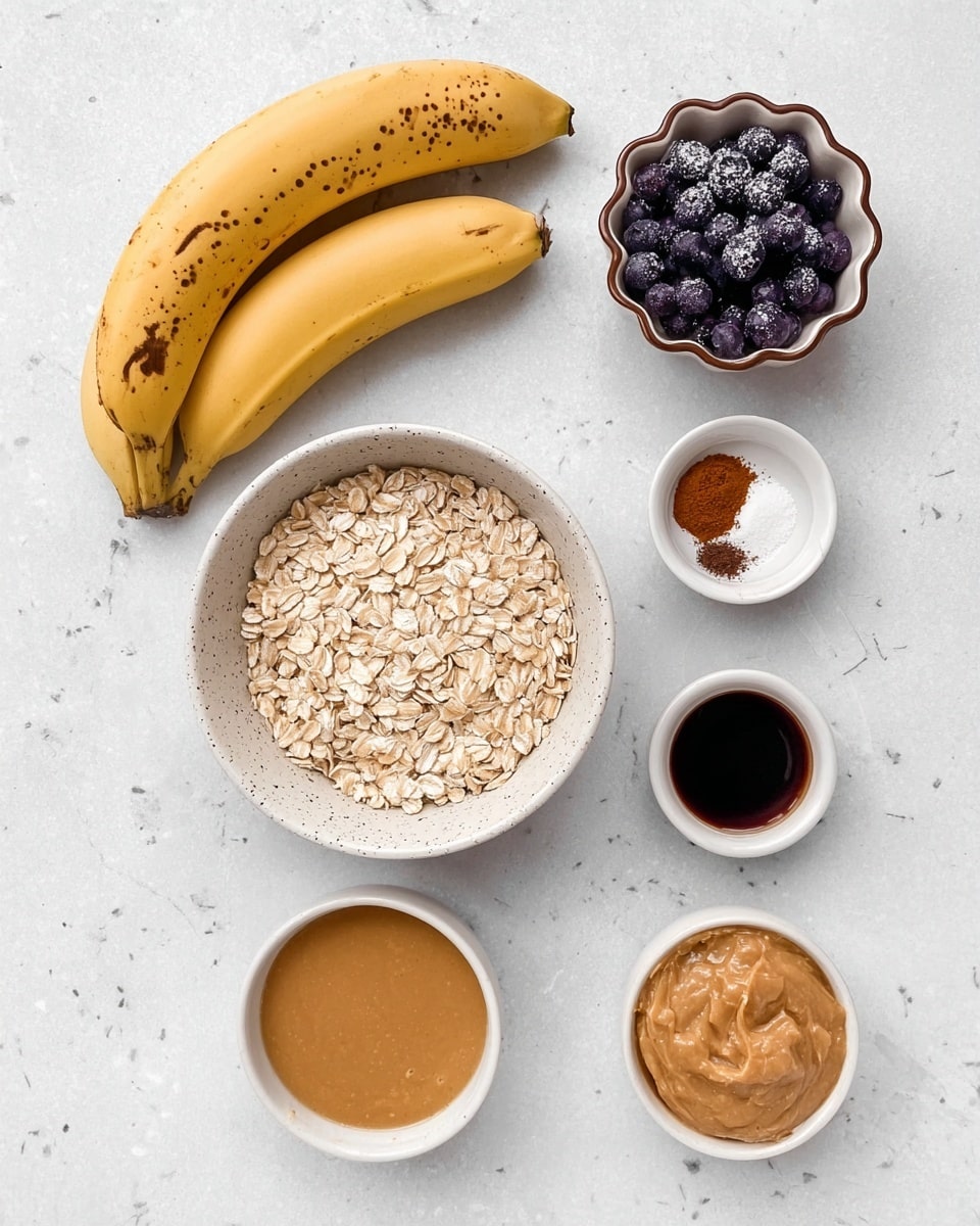 The image shows six ingredients arranged neatly on a white marbled surface. On the left, there are two ripe yellow bananas with brown spots. Near the center, a white speckled bowl is filled with light beige rolled oats. Above this, a small white bowl with a brown spiked edge holds dark purple blueberries dusted with frost. To the right, three small bowls are lined up vertically: the top one contains reddish-brown cinnamon powder, the middle one has a small amount of white salt, and the bottom one holds a dark brown liquid, likely vanilla extract. Below the oats, a white bowl contains smooth light brown peanut butter, and next to it, another white bowl holds beige applesauce with a slightly chunky texture. photo taken with an iphone --ar 4:5 --v 7