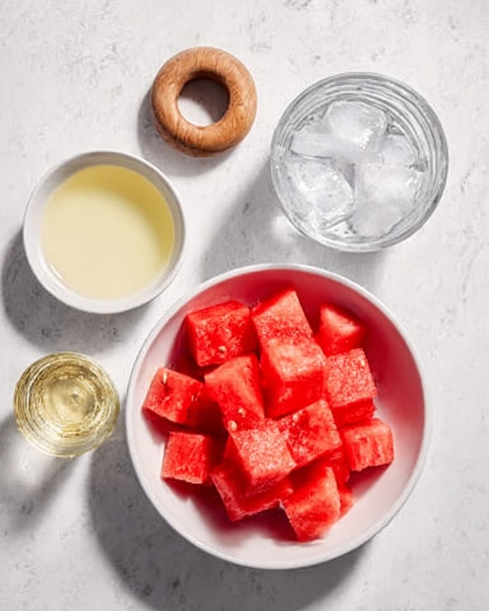 A white bowl filled with bright red watermelon cubes is placed on a white marbled surface. Next to it, there is a small white bowl with pale yellow juice and a glass with clear ice cubes. A small wooden ring-shaped object and a small clear glass filled with a transparent liquid are also arranged nearby. The scene is clean and simple with no extra decorations. Photo taken with an iphone --ar 4:5 --v 7