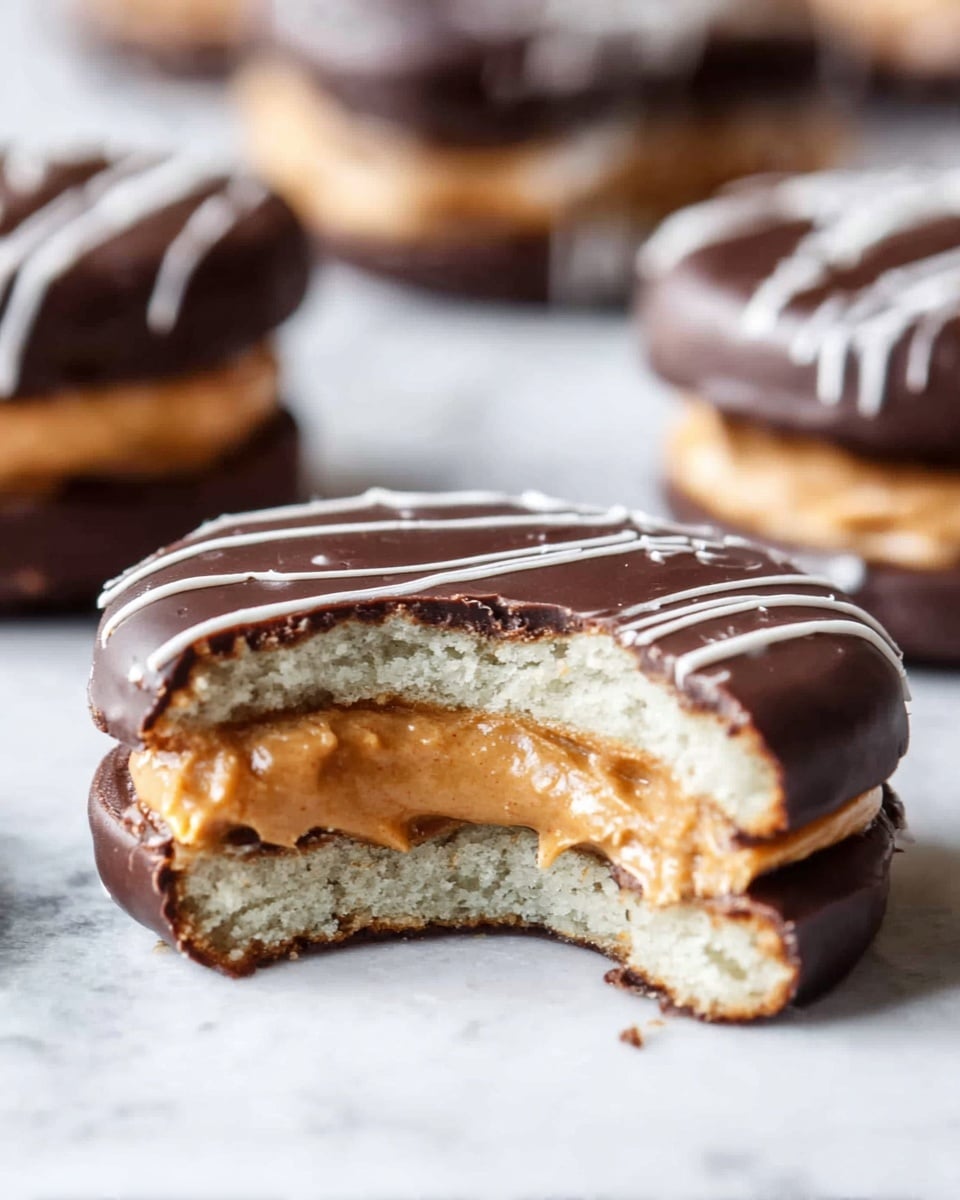 The image shows a close-up of a sandwich cookie on a white marbled surface, with a bite taken out to reveal its layers. The cookie has two round layers of light beige biscuit, slightly textured and soft in look. Between the biscuits, there is a thick layer of creamy peanut butter with a smooth and dense texture. Outside the cookie, there is a dark chocolate coating covering everything except a few thin white chocolate lines drizzled on the top, creating contrast. In the background, several whole covered cookies are slightly blurred. Photo taken with an iphone --ar 4:5 --v 7
