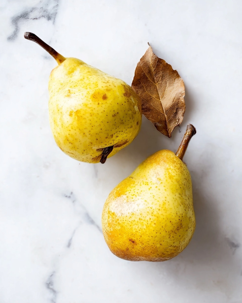 Two yellow pears with small brown spots are placed on a white marbled surface. One pear is positioned slightly below and to the left, showing its entire shape with a short brown stem. The other pear is above and to the right, showing its top side clearly with a dried brown leaf attached to the stem. The light highlights the smooth but speckled texture of the pears' skin. photo taken with an iphone --ar 4:5 --v 7
