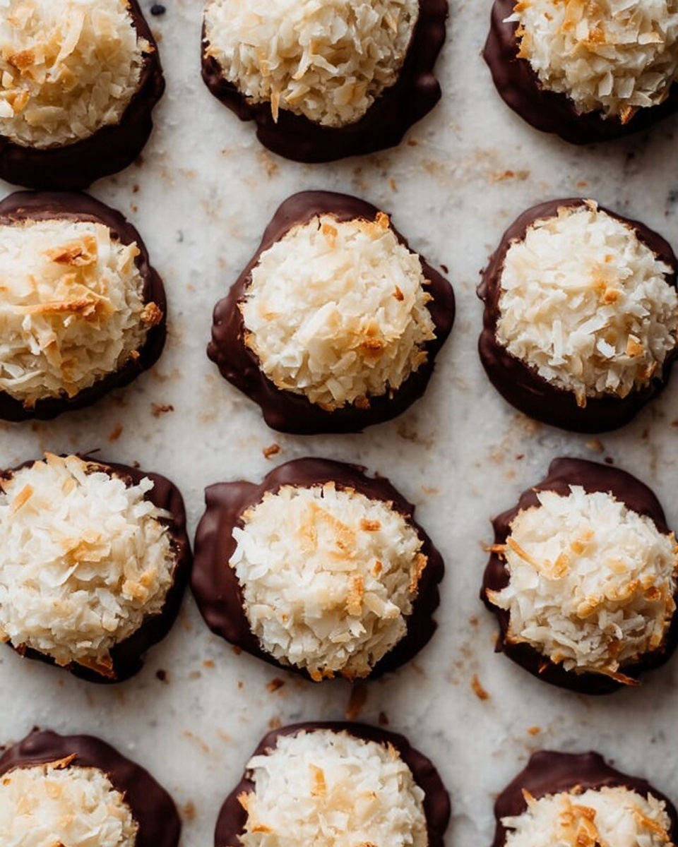The image shows round cookies arranged in rows on a white marbled surface. Each cookie has two layers: the top layer is a light, fluffy mound of shredded coconut, with slightly toasted tips giving a mix of white and soft golden colors. The bottom layer is dark chocolate that forms a thick, uneven base, slightly melted and spreading irregularly around the edges. The cookies are evenly spaced and have a rustic, homemade appearance. photo taken with an iphone --ar 4:5 --v 7