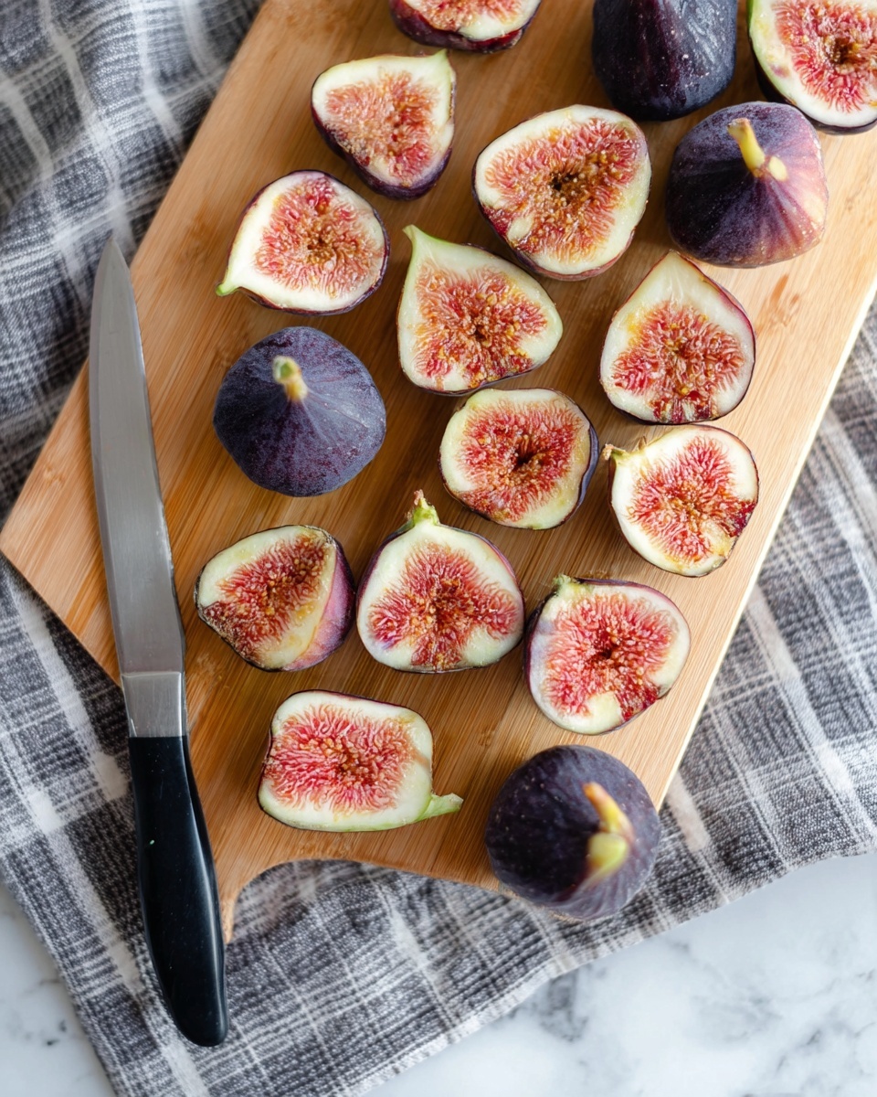 The image shows many figs, mostly cut in half, laid out on a wooden cutting board. Each fig half reveals a soft pink and light orange inner texture with small seeds, surrounded by dark purple skin. There are three whole figs with dark purple skin and a small green stem. A silver knife with a black handle is placed diagonally at the bottom center of the board. The cutting board is placed on a checkered gray and white cloth, which is on a white marbled textured surface. Photo taken with an iphone --ar 4:5 --v 7