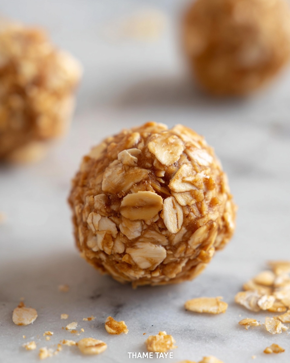 A close-up view of a single round oat ball with a rough texture made from oats and a golden brown dough, resting on a light surface with a white marbled texture. The oat ball is covered in whole oats that stick out unevenly, giving it a crunchy and chunky look. Around it, some loose oat flakes and small crumbs are scattered. In the background, two other oat balls are softly blurred, emphasizing the main oat ball in sharp focus. The lighting is soft and natural, enhancing the warm tones of the oats and dough. photo taken with an iphone --ar 4:5 --v 7