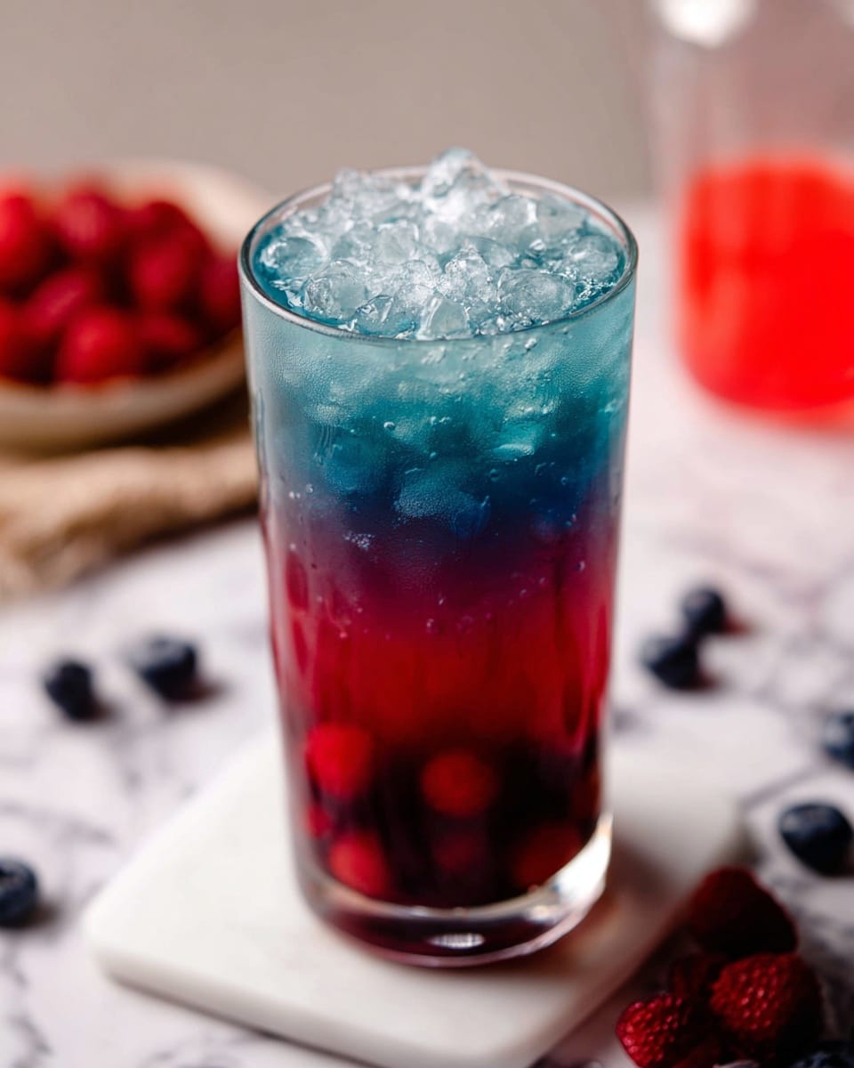 A tall clear glass filled with a colorful drink showing three layers: the bottom layer is deep red with round berry-like shapes, the middle layer is a dark blue fading upwards, and the top layer is light blue covered with many clear ice cubes. The glass sits on a white marble surface with some red and dark berries nearby. In the blurry background, there is a small clear container with a bright red substance. Photo taken with an iphone --ar 4:5 --v 7