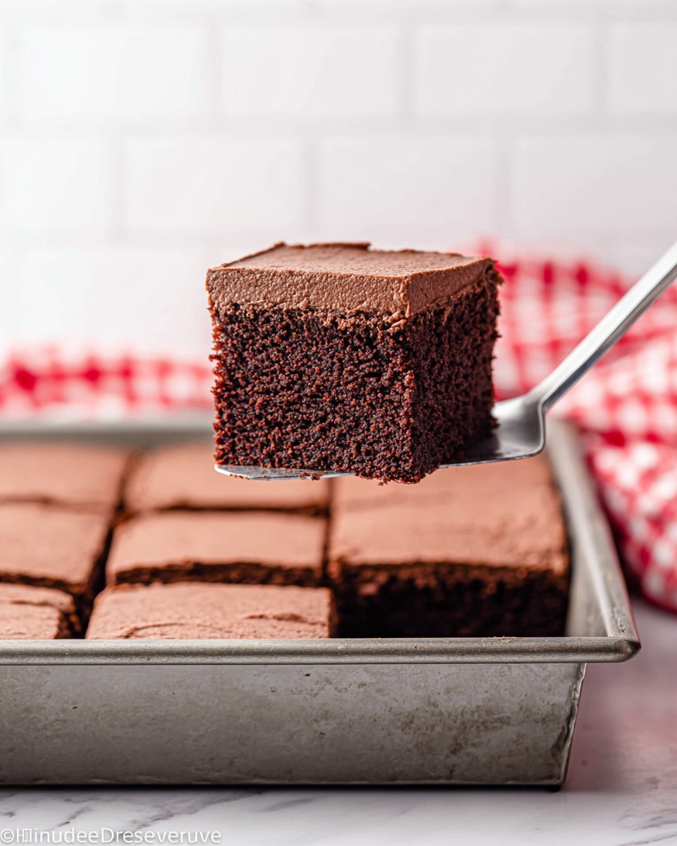 The image shows a thick single slice of chocolate cake being lifted from a rectangular metal baking pan. The cake has two layers: a moist, dark brown sponge base with a slightly rough texture, and a smooth, slightly lighter brown chocolate frosting layer on top. The pan is filled with several evenly cut square pieces of the same cake, sitting on a white marbled surface. A blurred red and white checkered cloth and white tiled background are visible behind the pan. Photo taken with an iphone --ar 4:5 --v 7
