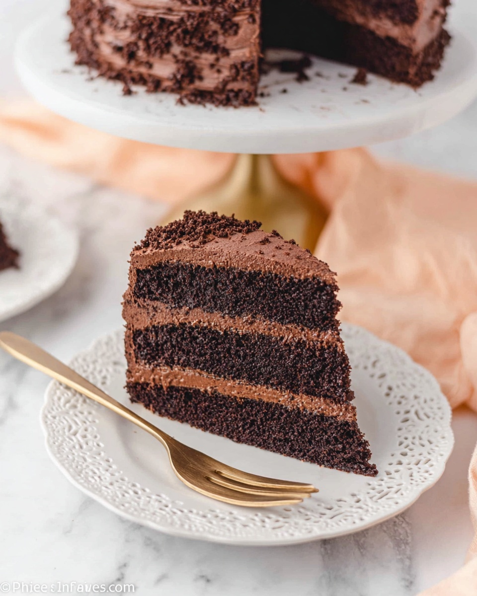 A slice of chocolate cake with three layers is shown on a white, lace-edged plate. The cake layers are dark brown and look soft, with thick, smooth chocolate frosting between each layer and around the outside. The outer frosting has small chocolate crumbs sprinkled on it, giving it a slightly rough texture. In the background, part of the whole cake on a white cake stand with gold legs is visible, and a light peach-colored cloth lies on a white marbled surface. A gold fork sits next to the cake slice on the plate. Photo taken with an iphone --ar 4:5 --v 7