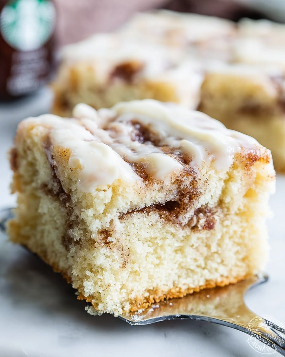 A close-up of a thick, square piece of light yellow cake with a soft, fluffy texture, showing layers of cinnamon brown swirls baked inside. On top, a creamy white glaze gently covers the surface, adding a smooth and shiny layer. The cake is on a metal spatula, with the edges showing a slight golden brown color from baking, all set against a soft white marbled textured background. Photo taken with an iphone --ar 4:5 --v 7