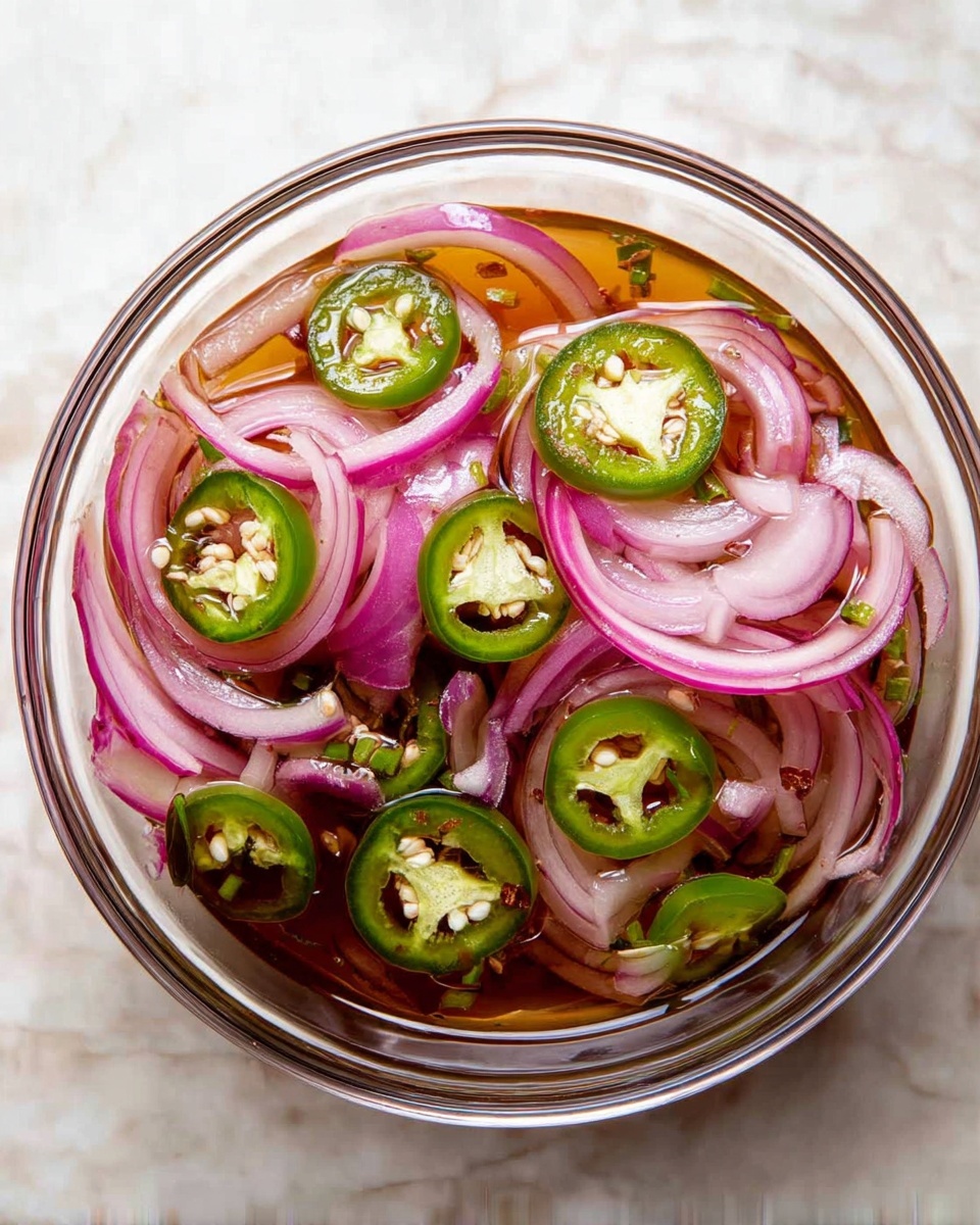 A clear glass bowl sits on a white marbled surface, filled with thin slices of purple-red onion layered with bright green jalapeño rings. The onions create soft, curved layers with a smooth, slightly translucent texture, while the jalapeños add a fresh, glossy look, scattered evenly on top, showing their seeds inside. The ingredients float in a light, amber-colored liquid that adds a shiny surface all around. photo taken with an iphone --ar 4:5 --v 7