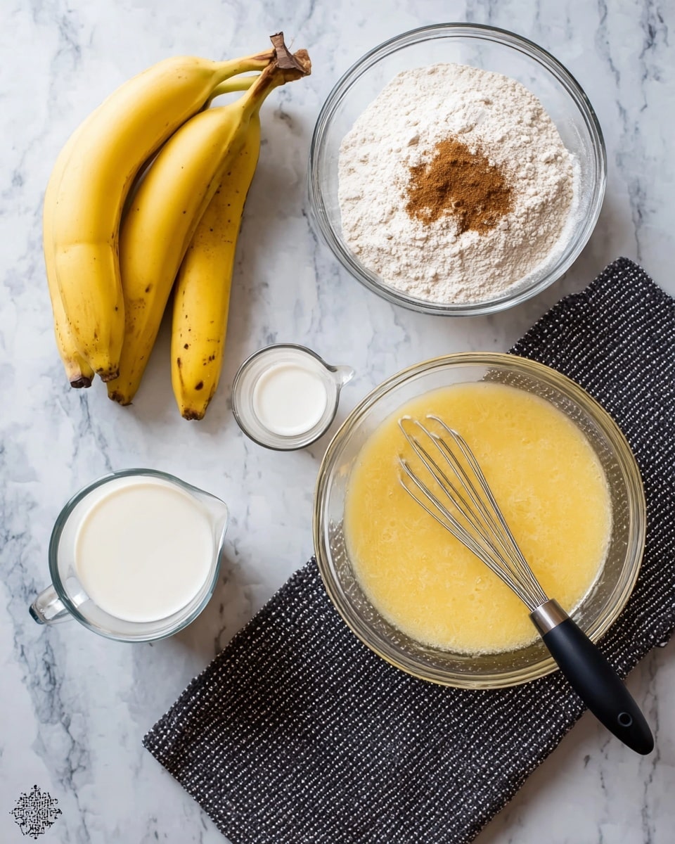The image shows four bananas lying in a small group on the left side on a white marbled surface. To the right on the top is a clear glass bowl filled with white flour and a small heap of brown spice on top. Below it, there is a small clear glass measuring jug with white milk inside. On the bottom left, there is a larger clear glass bowl with a yellow wet mixture and a whisk with a black handle resting inside. A dark gray textured cloth is placed to the right of the bowl on the white marbled surface. photo taken with an iphone --ar 4:5 --v 7