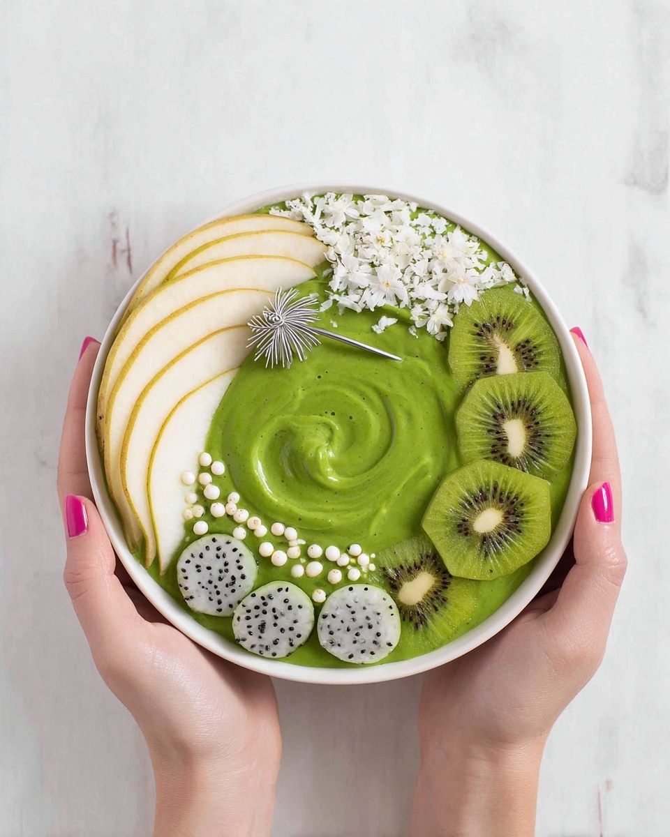 A white bowl is filled with a thick, bright green smoothie base that swirls slightly in the center. On the left side, thin slices of pale yellow pear fan out neatly above a small pile of white coconut flakes. On the right, five round slices of green kiwi cover the edge, with a small silver palm tree pick sticking out from the kiwi. Along the bottom curve, small round scoops of green kiwi and white dragon fruit with black seeds alternate, decorated further with tiny white edible pearls and two small white flowers. The bowl is held by two woman's hands with pink nail polish, all set against a white marbled surface. Photo taken with an iphone --ar 4:5 --v 7