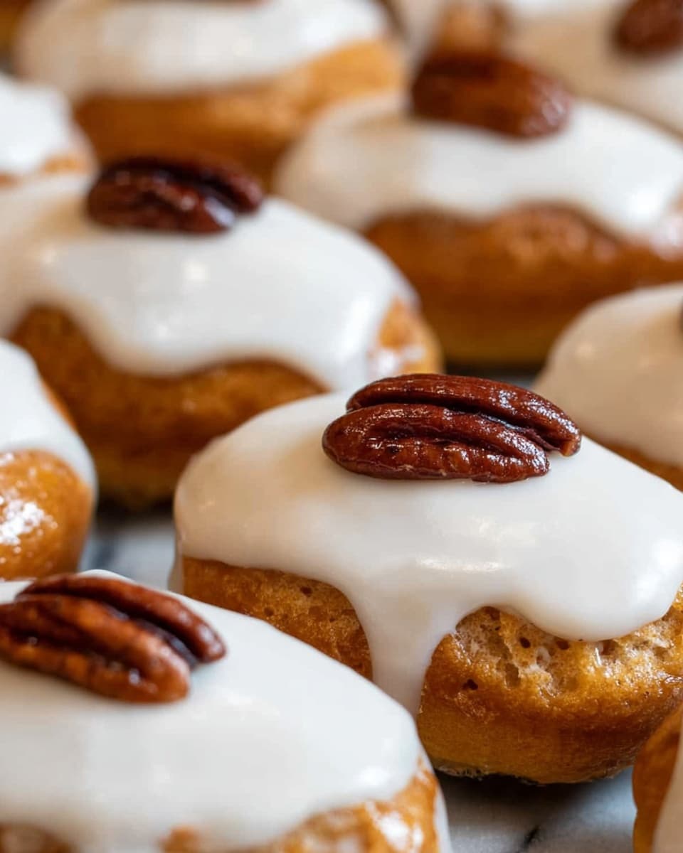 The image shows a close-up of small, oval-shaped pastries with a golden-brown base layer that looks soft and slightly shiny. Each pastry is topped with a thick, smooth white icing layer that covers the top surface completely. On top of the icing, there is one glossy, dark brown pecan placed in the center of each pastry. The background is a white marbled texture, making the pastries stand out clearly. The arrangement shows multiple pastries close together, highlighting the texture and shine of both the icing and pecans. photo taken with an iphone --ar 4:5 --v 7