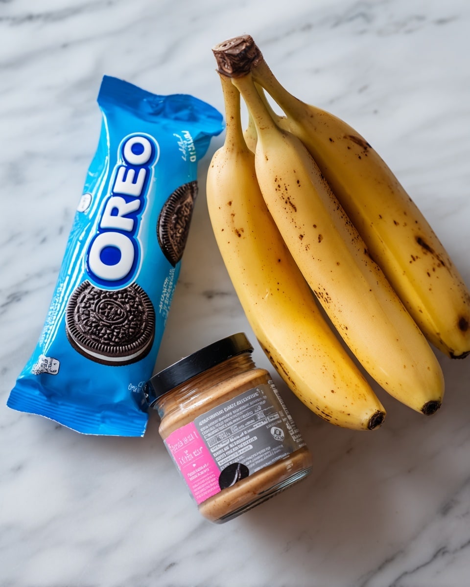 The image shows three main items placed on a white marbled surface. On the left side, there is a pack of Oreo cookies in bright blue packaging with white and black text. In the middle, there are three ripe bananas with yellow skin and some brown spots, lying close to each other with their curved shapes visible. On the right side, there is a small glass jar of cashew butter with a pink and white label and a black lid. The items are arranged in a row, each clearly separated from the others. The background is clean and light, adding focus to the objects. Photo taken with an iphone --ar 4:5 --v 7