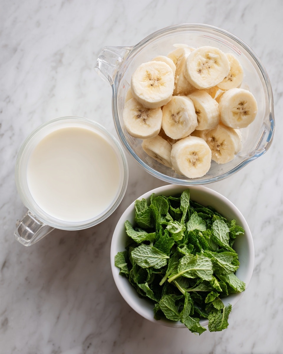 The image shows three containers with ingredients placed on a white marbled texture. One container is a clear measuring cup filled with frozen banana slices that are pale yellow with brown spots, filling about three-quarters of the cup. Another clear measuring cup holds a creamy white liquid that looks smooth and slightly thick, almost full. The third container is a small white bowl filled with fresh green mint leaves, vibrant and slightly glossy, loosely packed. The arrangement is simple, with the white bowls creating a clean look against the marbled background. photo taken with an iphone --ar 4:5 --v 7