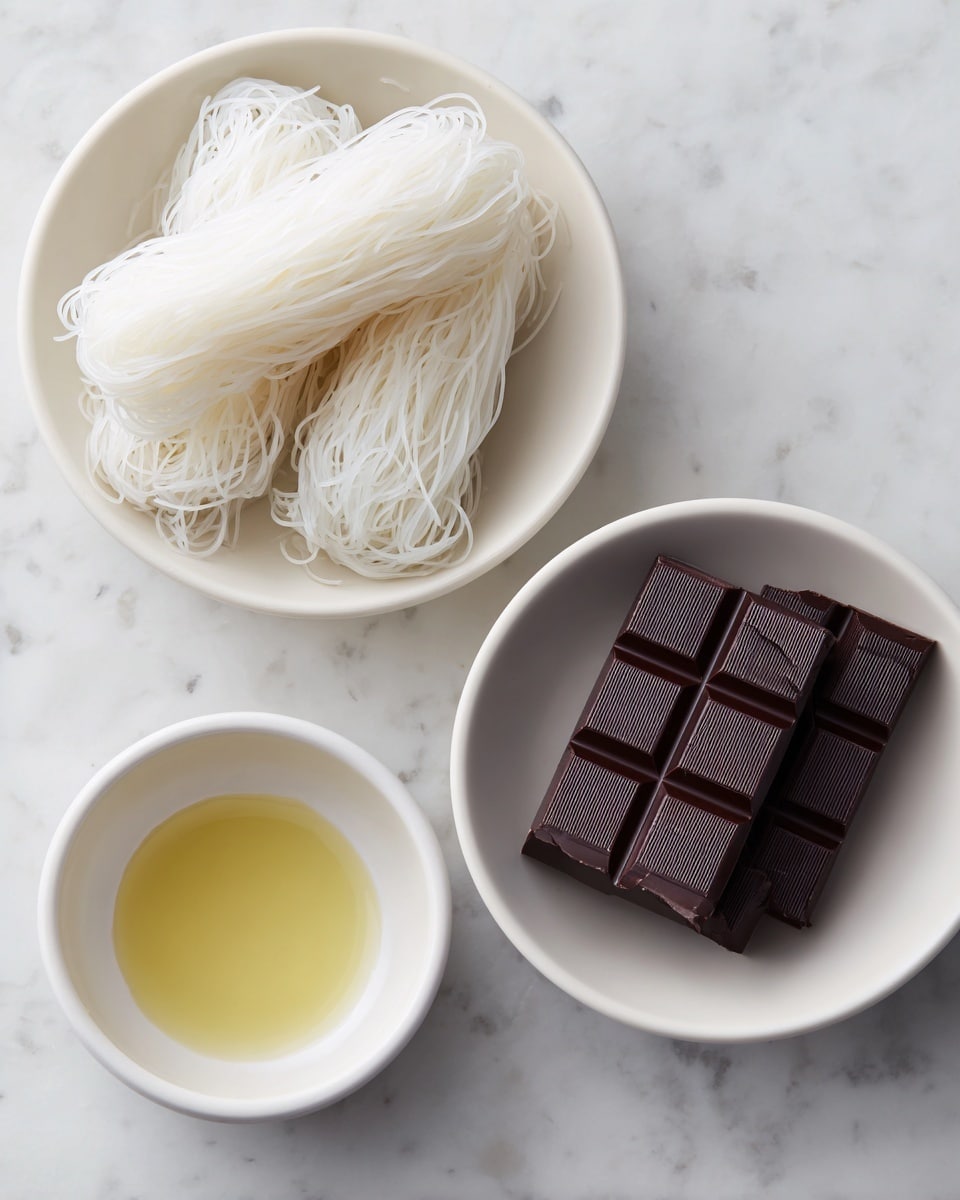 The image shows three white dishes arranged on a white marbled surface. The largest bowl on the left holds two bundles of thin, white translucent noodles with a string tied loosely around each. On the right, a medium-sized white bowl contains two dark brown chocolate bars, each divided into six rectangular pieces with faint writing on top. Below these two bowls is a small white bowl filled with a clear yellow liquid, likely oil, with a smooth surface and soft reflections. The overall color palette is neutral with light whites and dark browns, showing a simple, clean food preparation scene. photo taken with an iphone --ar 4:5 --v 7