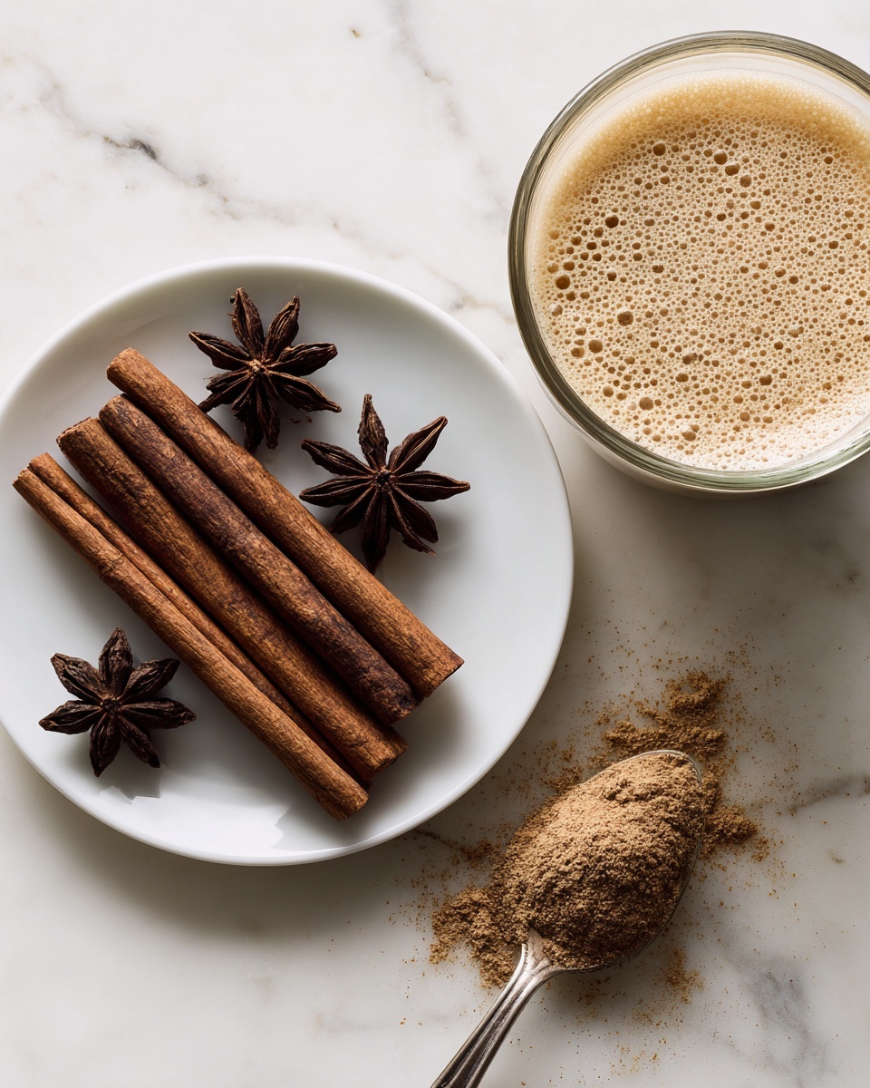 A small white plate holds seven long dark brown cinnamon sticks arranged side by side, with three star anise pods placed on top, each showing a detailed star shape and dark brown color. To the right, there is a glass measuring bowl filled halfway with a frothy beige liquid, its surface showing small bubbles. Below the bowl on the same white marbled surface lies a tarnished silver spoon heaped with light brown powdered spice, with some powder scattered around it. The overall scene is closely shot, showing rich texture on all spices. Photo taken with an iphone --ar 4:5 --v 7