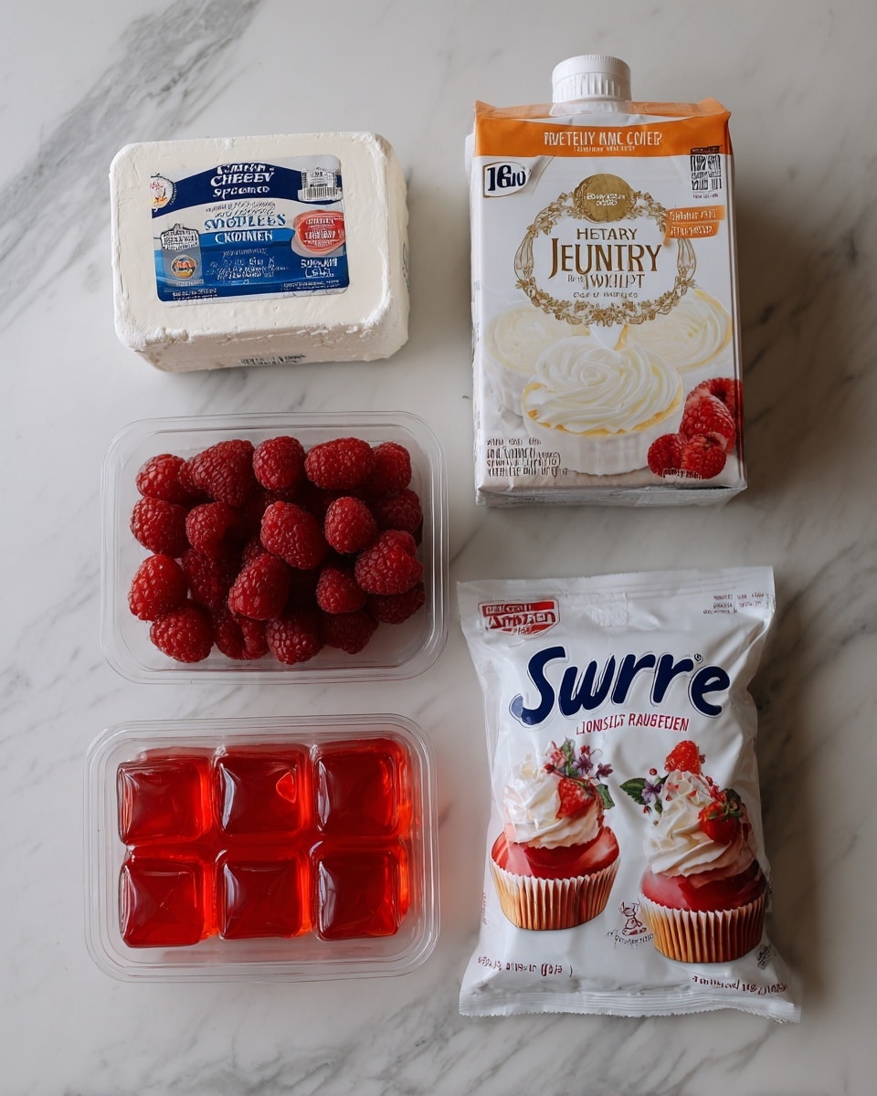 The image shows a flat lay of six items arranged on a white marbled surface. At the top left is a rectangular block of cream cheese in white packaging with blue and red text. To its right is a carton of heavy whipping cream with a cream-colored and red label featuring an image of whipped cream. Below these, on the left, is a clear plastic container filled with bright red raspberries. To the right of the raspberries is a white bag of sugar substitute with the brand name